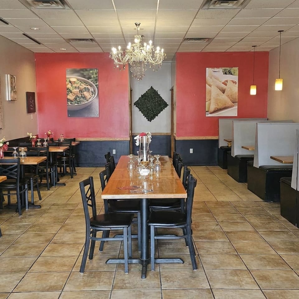 Empty restaurant dining room with wooden tables, black chairs, booth seating, colorful food artwork, and chandeliers.