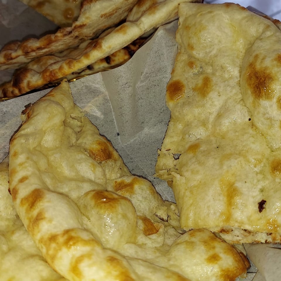 Basket of golden-brown baked flatbreads, including folded and elongated pieces, resting on parchment-lined serving trays.