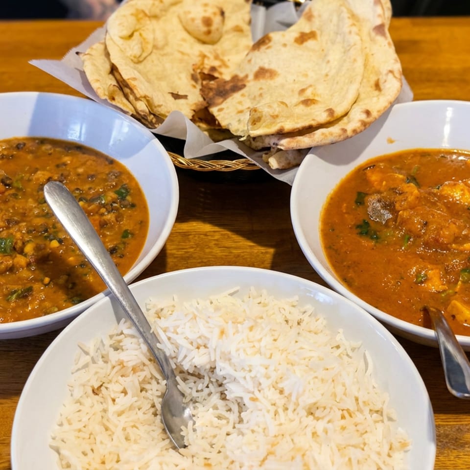 Indian meal featuring bowls of lentil curry, chicken curry, basmati rice, and naan bread on a wooden table.