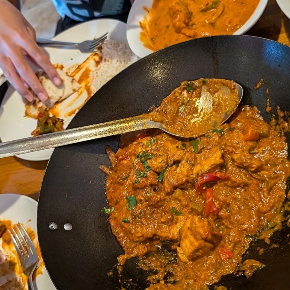 Indian curry served in a black pan with naan, basmati rice, and additional dishes on a restaurant table.