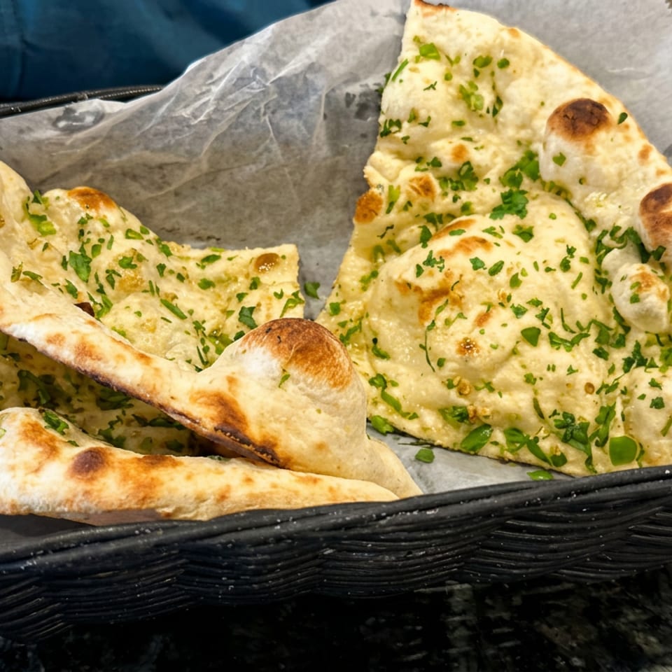 Basket of freshly baked garlic naan breads garnished with chopped cilantro on a dining table.