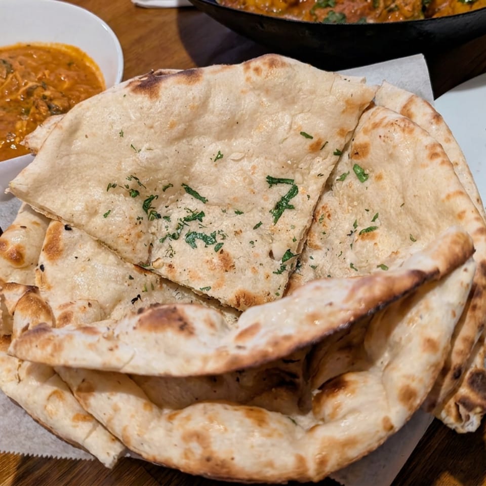 Stacked naan breads garnished with herbs beside bowls of creamy curry on a restaurant table.