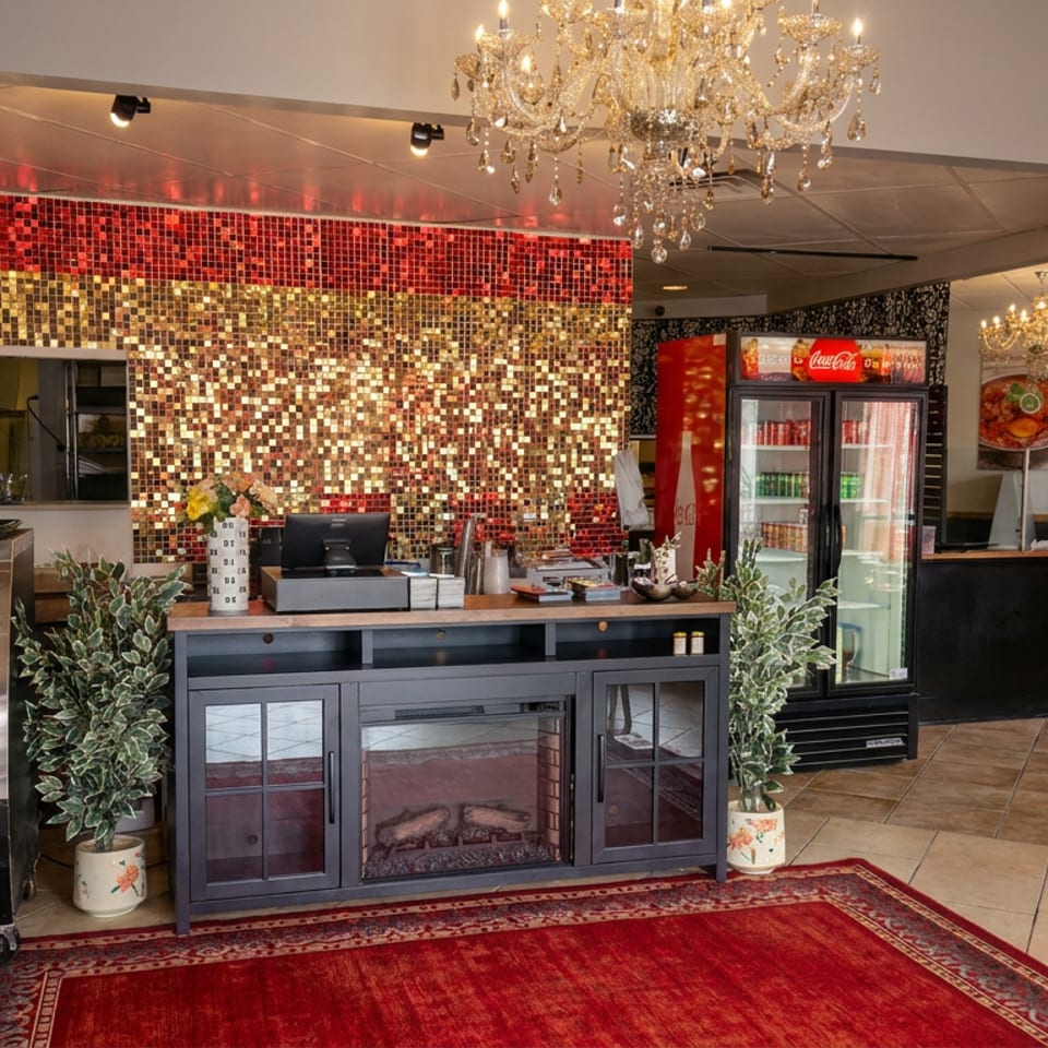 Elegant restaurant interior featuring a red-and-gold mosaic wall, crystal chandeliers, refrigerated display case, counter, and dining tables.