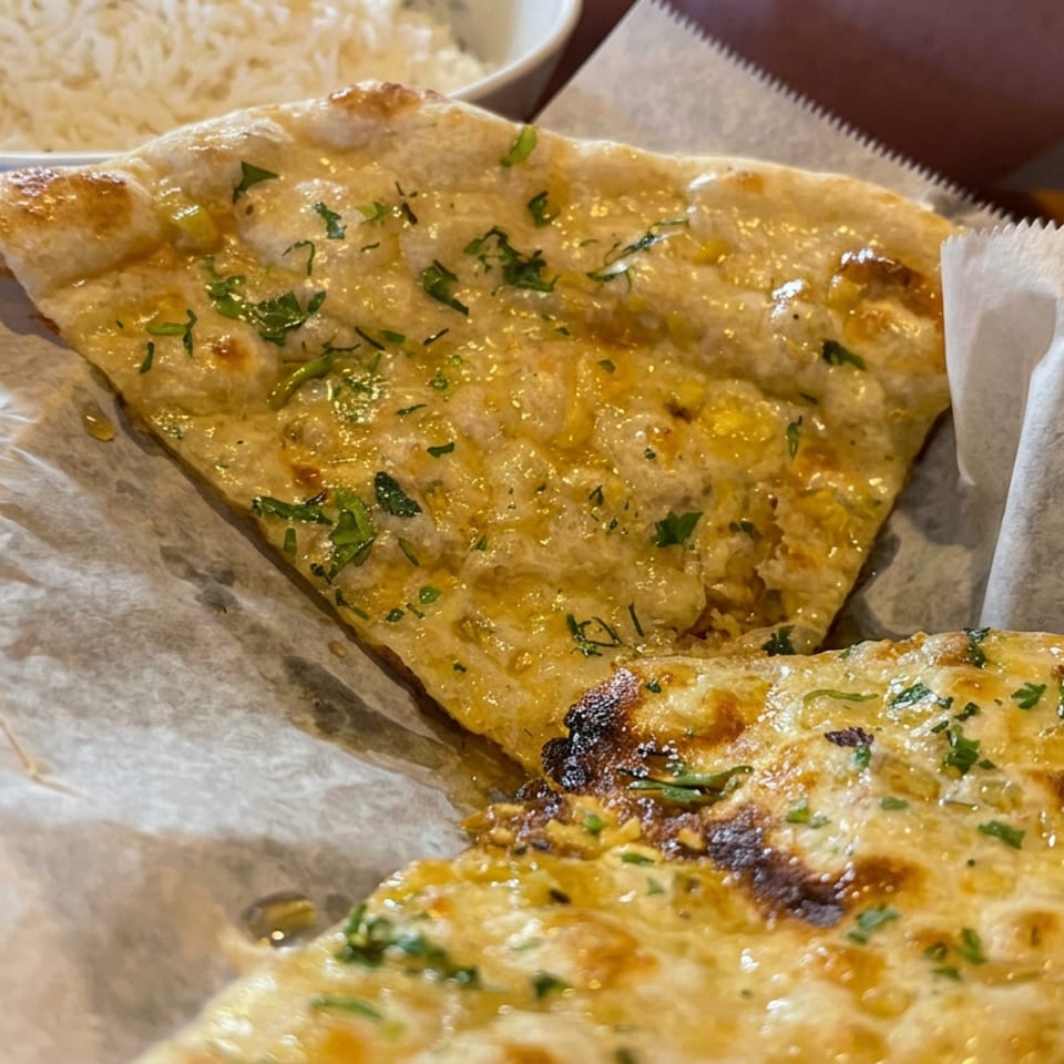 Two golden, herb-topped flatbreads served on parchment beside a bowl of rice on a wooden table.