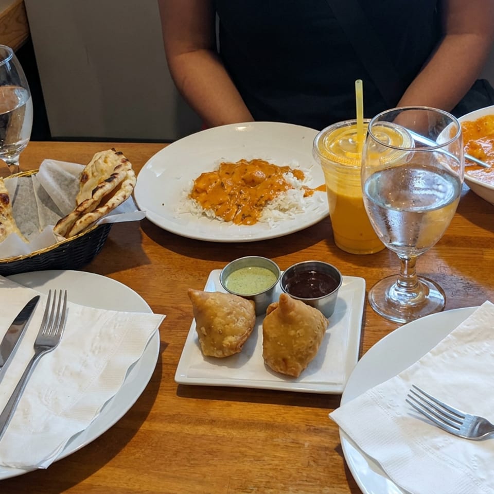 Indian meal spread with naan, rice and curry, samosas with chutneys, drinks, and table settings in a restaurant.