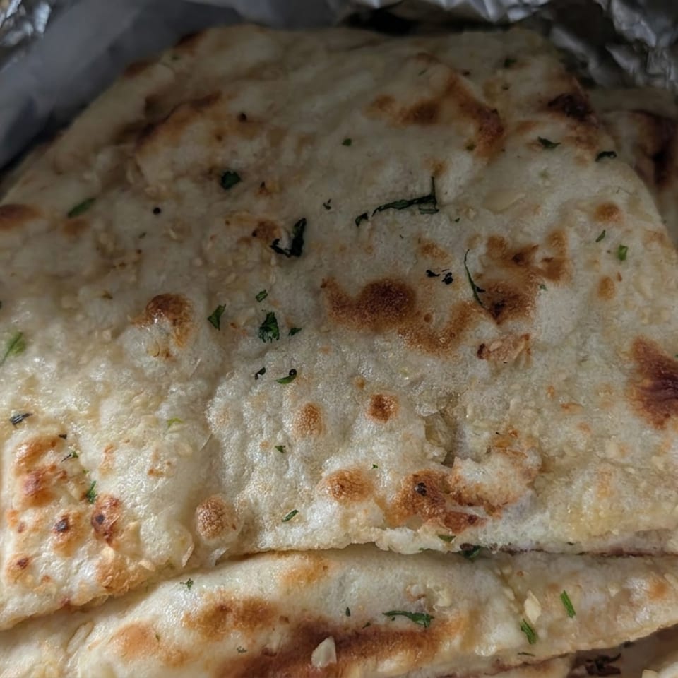 Stack of golden-brown, herb-speckled flatbreads wrapped in crinkled aluminum foil.